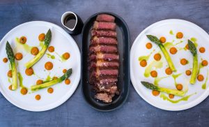 Wagyu Beef Steaks Complimented By Two Plates of Asparagus.